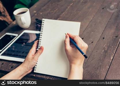 Woman hand writing note pad on wood table in coffee shop.