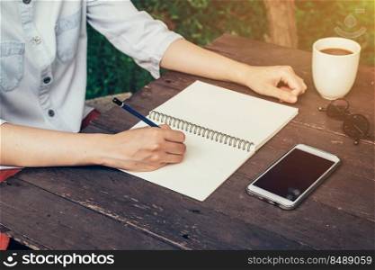 Woman hand writing note pad on wood table in coffee shop.