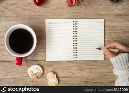 Woman hand writing on notebook with black coffee cup and Christmas cookies on table. Xmas, Happy New Year, Goals, Resolution, To do list, Strategy and Plan concept
