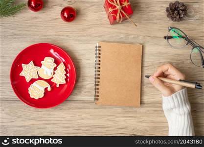 Woman hand writing on notebook with Christmas cookies on table. Xmas, Happy New Year, Goals, Resolution, To do list, Strategy and Plan concept