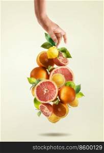 Woman hands and various falling citrus fruits with green leaves at pale beige background. Grapefruit, lemon, orange and lime flying in the air. Healthy food concept.