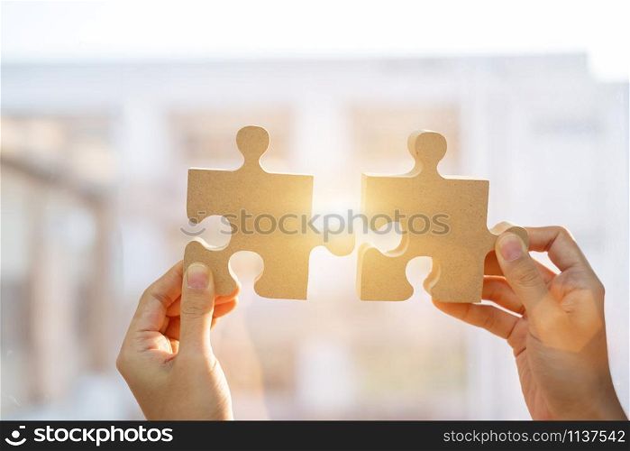 Woman hands connecting couple puzzle piece against sunrise effect, businesswoman holding wood jigsaw with sunset background. Business solutions, target, success, goals and strategy concepts