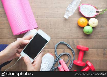 Woman hands holding mobile phone, Sport equipments and fruits on wooden floor