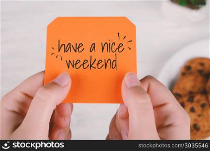 "Woman hands holding note paper with text "have a nice weekend" and cookies. Focus on paper. Woman hands holding note paper with text "have a nice weekend" "