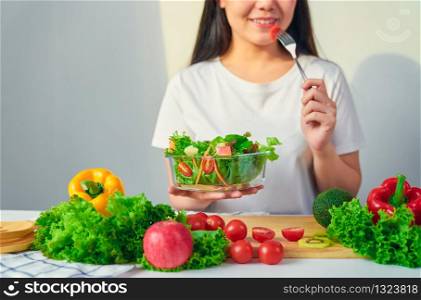 Woman hands holding salad bowl with eating tomato and various green leafy vegetables on the table at the home.