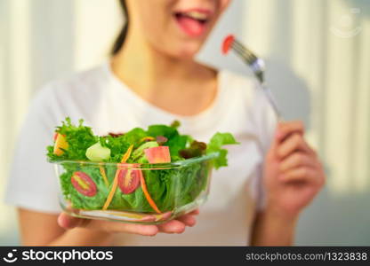 Woman hands holding salad bowl with eating tomato and various green leafy vegetables on the table at the home.