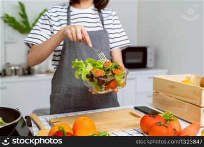Woman hands holding salad bowl with eating tomato and various green leafy vegetables on the table at the home.