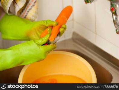 Woman hands in green gloves slicing preparing carrots in kitchen, indoor. Healthy diet, organic nutrition. Realistic, natural image.