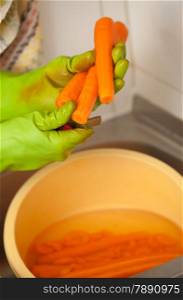 Woman hands in green gloves slicing preparing carrots in kitchen, indoor. Healthy diet, organic nutrition. Realistic, natural image.