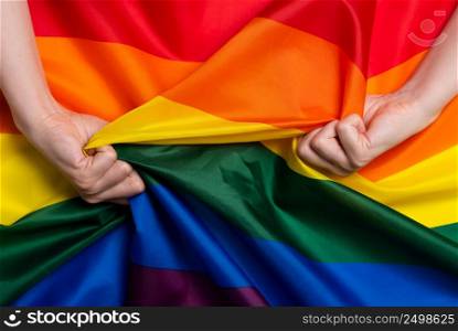 Woman hands pull rainbow Pride flag concept top view