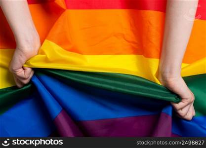 Woman hands pull rainbow Pride flag sign concept top view
