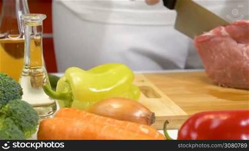Woman hands slicing fresh raw meat for cooking with vegetables in kitchen. Dolly shot.