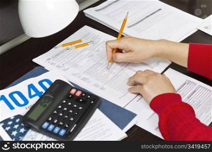 Woman hands with pencil eraser, calculator, lamp, tax forms on desk top