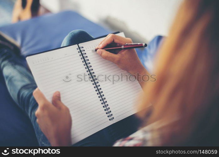 Woman hands writing on notepad lying at home . 