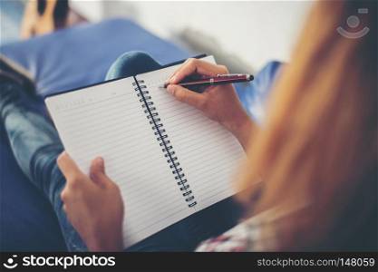 Woman hands writing on notepad lying at home . 