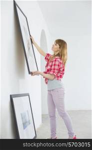 Woman hanging picture frame on wall in new house