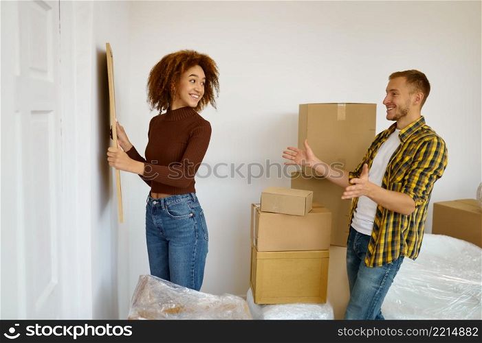 Woman hanging picture on the wall surrounded cardboard boxes with belongings prepared for resettlement. Woman hanging picture on the wall