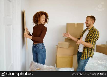 Woman hanging picture on the wall surrounded cardboard boxes with belongings prepared for resettlement. Woman hanging picture on the wall