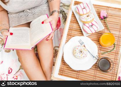 woman having breakfast in bed while reading a book