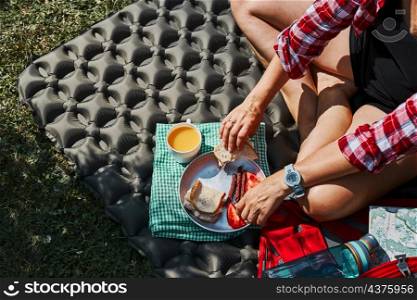 Woman having breakfast sitting by tent at camping. Female actively spending summer vacations close to nature outdoors. Concept of camp life