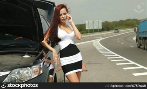 Woman having car troubles on the road, calling on the cell phone for emergency repair service.