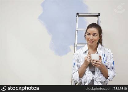 Woman having coffee by half-painted wall