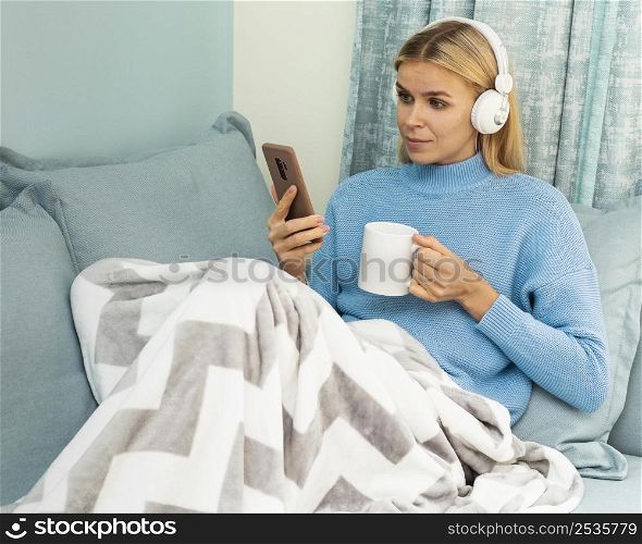 woman having coffee home while using smartphone headphones during pandemic