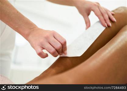Woman having hair removal procedure on leg applying wax strip depilatory in salon. Depilation concept