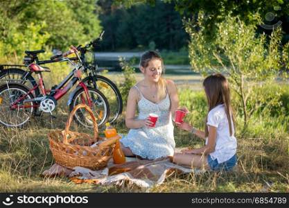 Woman having picnic by the river with 10 years old daughter. Two bicycles on the background