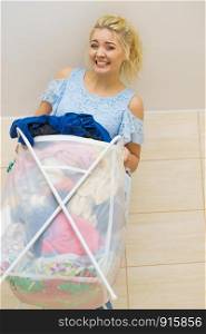 Woman having troubles with holding big laundry basket full of colorful dirty clothes. Bathroom utensils concept.. Woman holding laundry basket full of clothes