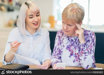 Woman Helping Confused Senior Neighbor With Paperwork And Domestic Finances