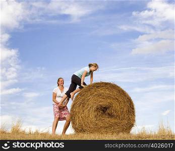 woman helping girl to climb hay bale