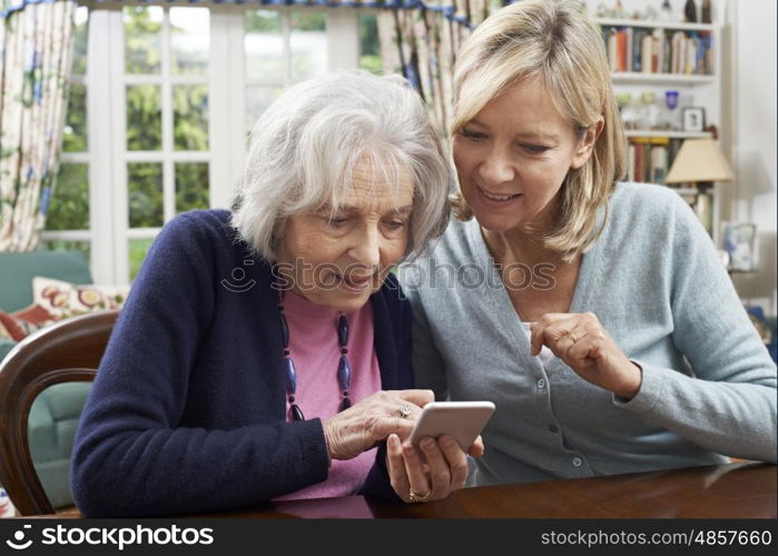 Woman Helping Semior Neighbor To Use Mobile Phone