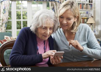 Woman Helping Semior Neighbor To Use Mobile Phone