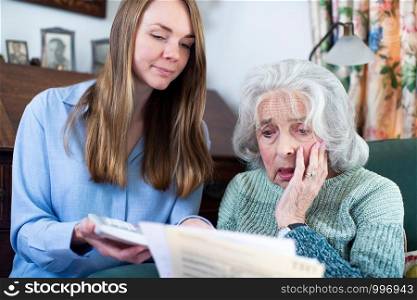 Woman Helping Worried Senior Neighbor Concerned About Debt With Bills And Paperwork