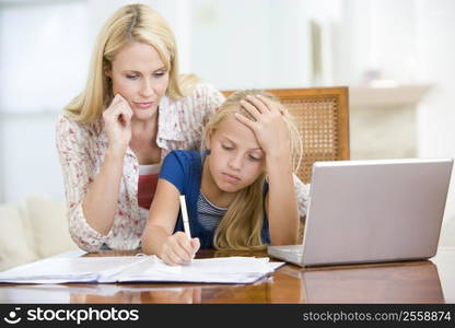 Woman helping young girl with laptop do homework in dining room