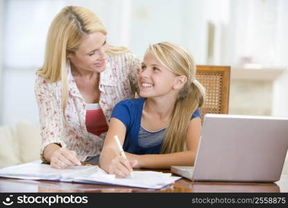 Woman helping young girl with laptop do homework in dining room