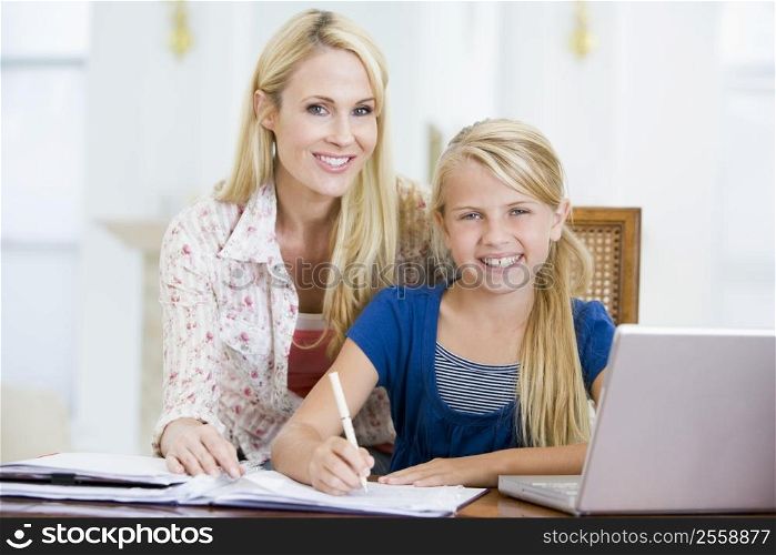 Woman helping young girl with laptop do homework in dining room