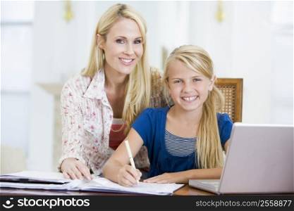 Woman helping young girl with laptop do homework in dining room