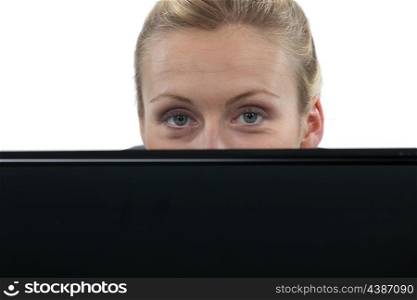Woman hiding behind laptop computer