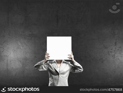 Woman hiding behind paper sheet. Unrecognizable businesswoman holding paper covering her face