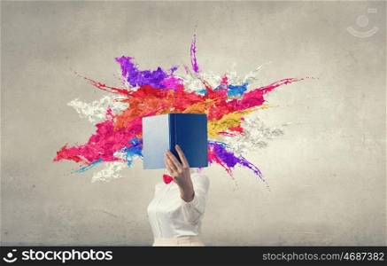 Woman hiding face behind book. Woman with opened book against her face and colorful splashes flying out