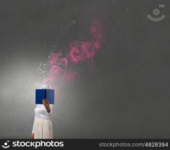 Woman hiding face behind book. Woman with opened book against her face and colorful light coming from pages