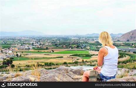 Woman hiker sitting on top of a mountain and relax in sunny summer day. Woman hiker sits on top of a mountain and relaxes while eating an apple.