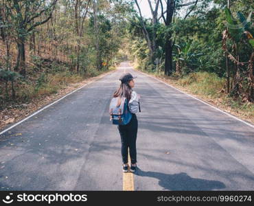 Woman hiking with backpack walking on roadway amid greenery trees. Girl are happy and cheerful while traveling.