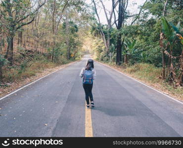 Woman hiking with backpack walking on roadway amid greenery trees. Girl are happy and cheerful while traveling.