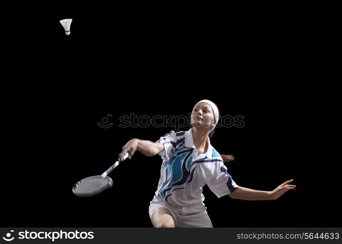 Woman hitting shuttlecock with badminton racket isolated over black background