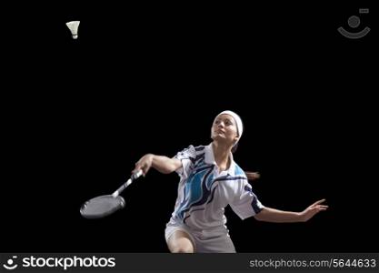Woman hitting shuttlecock with badminton racket isolated over black background