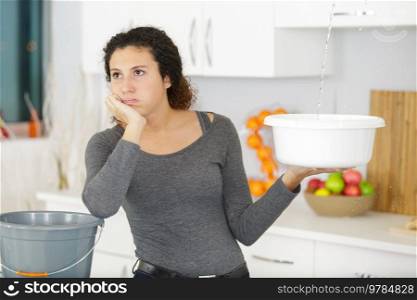 woman holding a bucket while water droplets leaking from ceiling
