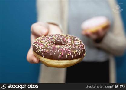 Woman holding a delicious colorful donut with sprinkles and giving the donut away, sharing near blue background. Woman holding a delicious colorful donut with sprinkles and giving the donut away, sharing
